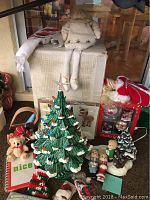 Full lot featuring large ceramic Christmas tree, snowman doll, Santa figurine, teddy bear, and assorted holiday decor on table.