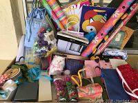 Photo showing various rolls of colorful wrapping paper, assorted gift bags, ribbons, bows, and boxes arranged together.