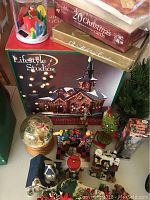 Top view of the Christmas village collection showing Lifestyle Studios church building in box, snow globe, candle, and various holiday figurines.