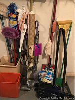 Wide view showing assortment of cleaning tools including mops, duster, brooms, a Regina electromechanical fan, and unopened cleaning cloths.
