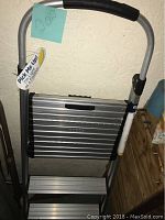 Aluminum folding stepstool in a folded position showing handle with cushioned grip, ribbed surface, and side supports