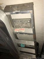 Taller metal ladder leaning against a wall showing the step construction and wear.