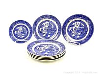 Seven blue and white vintage china plates featuring 'Willow' pattern, four dinner plates and one salad plate arranged for display