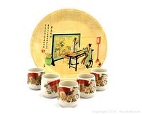 Photo showing a round Chinese bamboo plate with traditional artwork and six floral Japanese ceramic cups.