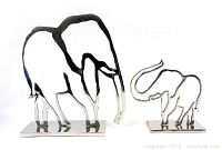 Front view of two metal elephant cut-out sculptures on rectangular bases showing their shiny polished metal surfaces and minimalistic design.