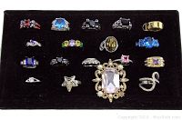 Photo of 18 assorted semi-precious stone rings on black display tray showing variety of styles and stones including blue, purple, pink, black, green, and gold tones.