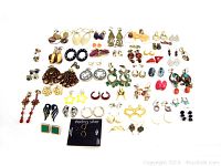 Flat-lay photo showing all 50 pairs of earrings arranged in rows on a white background, featuring various colors and styles including gold-tone, silver-tone, enamel, and novelty shapes.