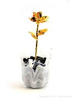 24kt gold dipped rose with detailed petals and leaves set in a white and grey swirled vintage art glass vase with black decorative stones.