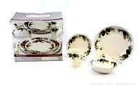 Photo showing the entire 16-piece set including plates, bowls, and mugs with pinecone pattern, and the original box with branding and pattern visible.