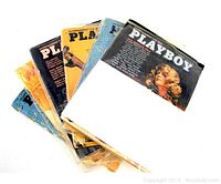 Six vintage Playboy magazines stacked with visible colorful and worn covers, showing a woman on the front cover of the visible top magazine.