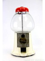 Front view of vintage gumball machine showing clear glass globe, red top, white base, and coin slot with turning handle on metal front.
