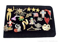 Photo showing a mix of 20 vintage brooches laid out on black velvet background. Various motifs including animals, stars, religious symbols, holiday characters.
