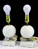 Pair of vintage hobnail milk glass accent lamps with round hobnail bodies and square hobnail bases, gold-tone sockets, and white bulbs, cords wrapped.