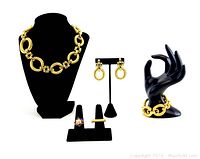 Full view of 5 piece jewelry set including gold-tone chunky link necklace on black bust, matching earrings on stand, matching chunky link bracelet on hand mannequin, plus two rings on ring holders.