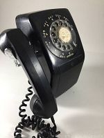 Side angle view of the black rotary dial phone showing the handset resting on the cradle and the rotary dial with numbers and letters.