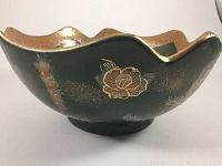 Side view of bowl showing green surface with gold floral designs and scalloped rim with gold edging.