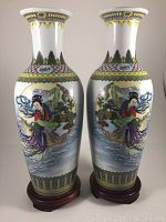 Pair of two tall porcelain vases each on a wooden base showing full front view with moon goddess motif and decorative borders.
