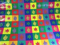 Wrapping paper showing colorful Hanukkah themed design with dreidel and Star of David shapes arranged in a checkerboard pattern.