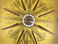 Full front view of mid-century electric starburst wall clock against yellow backdrop, showing 25.75 inch diameter with wooden rays and curled metal rods.