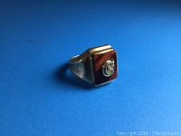 Front view of the gold ring showing the rectangular reddish-brown stone inlay with a raised initial 'C'.