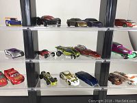 Photo of three shelves of Hot Wheels cars displayed securely on clear plastic stand, showing variety of styles and colors.