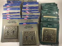 Overview of all switch plates showing unopened packaging and quantity with separation between ornate Taiwanese and lacquered brass Canadian plates.