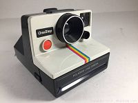 Front angled view showing the camera body, lens, rainbow stripe and shutter button