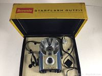 Open box with Kodak Brownie Starflash camera, flash, flash cord, and strap inside