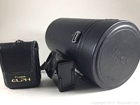 Nikon lens case 5in diameter and 10in tall, black cylindrical with strap, Canon ELPH camera case black leather with gold lettering.