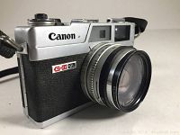 Front angled view of Canon Canonet QL17 G-III 35mm film camera showing lens, part of body with the Canon logo and strap mounts.