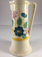 Front view of the cream ceramic pitcher showing blue and purple flowers with green leaves, yellow band near base, and crazing on the surface.