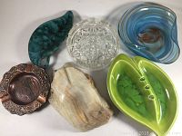 Six assorted ashtrays of different materials, shapes and colors on white background