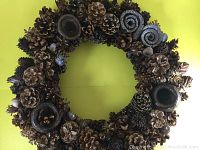 Full view of the circular pine cone wreath against a green background, showing the varied sizes and types of pine cones attached to the wreath base.