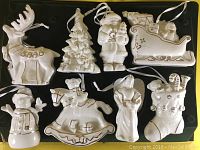 Top-down view of all 8 white and gold porcelain Christmas ornaments arranged flat on a dark surface.