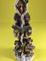 Full front view of the figurine showing Seraphina wearing a thick snow-covered hooded coat, holding an open book, with two children reading at her feet.