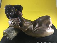 Full profile view of reclining female statuette lying on pillow-shaped base