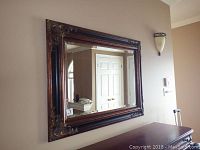 Wall mirror reflecting room interior, showing ornate frame and beveled glass.