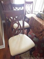 Three wood dining chairs with carved backs and cream upholstered seats.