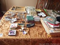 Photo showing assorted stainless steel cutlery, paper napkins (new sealed and some opened), placemats, and kitchen utensils arranged on a table.