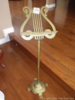 Full view of the music stand showing the lyre-shaped top, brass rods, and stand height on a hardwood floor.