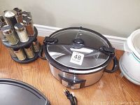 Photo of electric grill, crock pots, and spice rack arranged on floor near wall