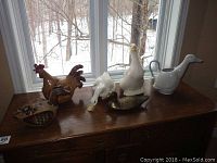 Photo showing all six bird-themed decorative items displayed on wooden furniture in front of window with snowy outdoor view.