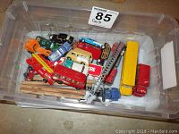 Top view of plastic bin containing a variety of die-cast model vehicles including fire truck, cars, a tractor, and trucks in HO scale for model railway.