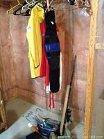 Wide view of back support belt, yellow rain jacket, fishing rods with reels hanging and on floor, badminton rackets inside blue bag on floor