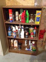 Front view of faux wood bookcase filled with various cleaning supplies including powders, sprays, liquids, and boxes.