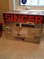 Front view of the boxed Singer sewing machine with prominent red Singer logo and image of the sewing machine.