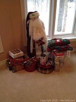 Overall view showing tall Santa, charger plates in red and gold, star lights, ornaments, stacked Christmas tablecloths and runners.