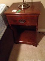 Night table showing drawer and open shelf, wooden construction, dark finish, with visible wear marks on top surface