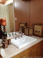 Bathroom sink area with waste basket, liquid soap dispenser, toothbrush holder, soap dish, cup, three framed prints, and candle holder visible exhibiting brown and beige ornate pattern design