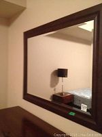 Full view of the rectangular wall mirror hanging on a light-colored wall, showing the dark brown frame and clear reflective surface.